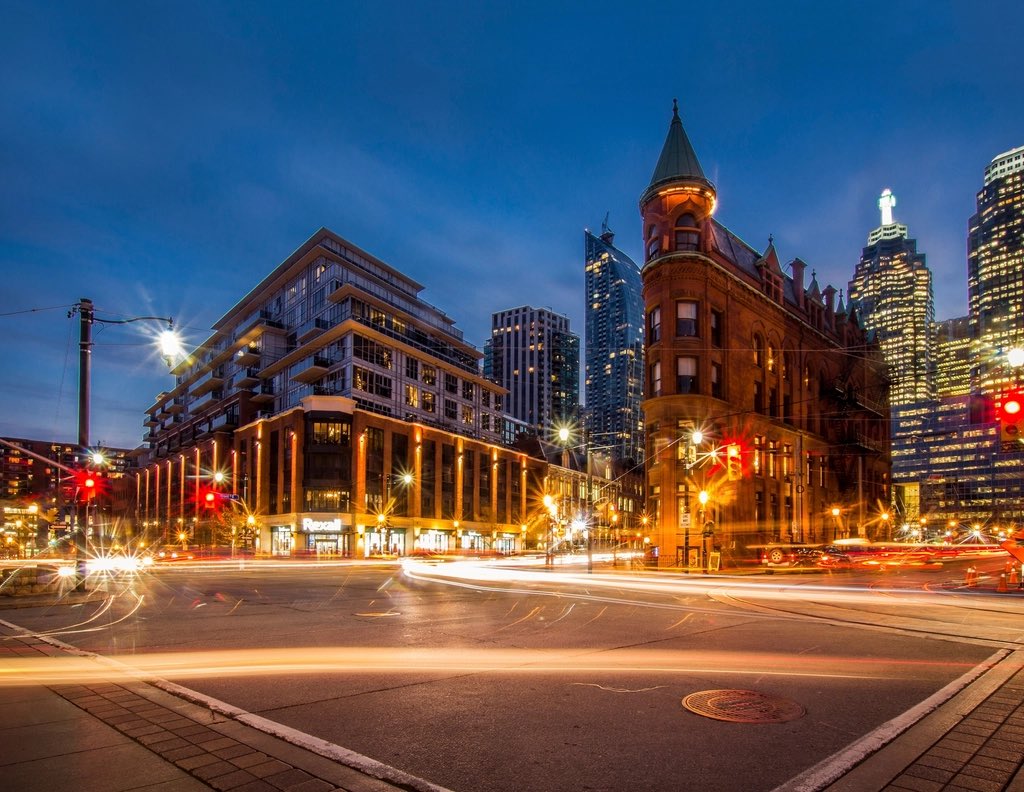 A downtown intersection at dusk: traffic lights on red and the light trails of cars turning across the crosswalk